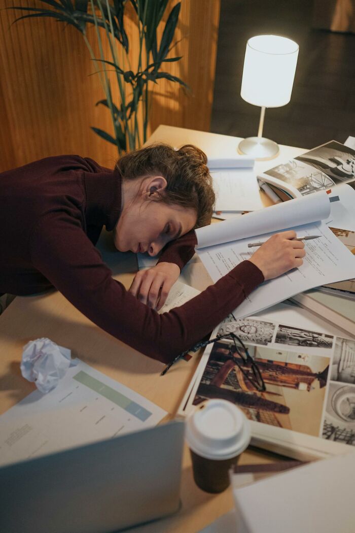 Woman exhausted and resting head on desk surrounded by papers, illustrating people sharing mysterious medical issues.