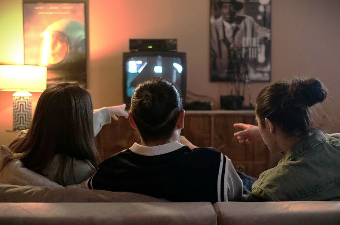 Three people sitting on a couch pointing at a TV screen, enjoying iconic TV show opening credits together.