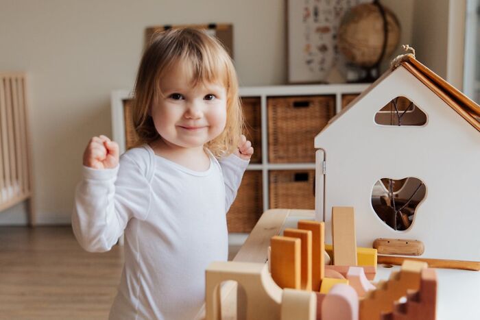 Toddler smiling and playing with wooden toys in a bright room, capturing funny and serious moments of raising monsters.