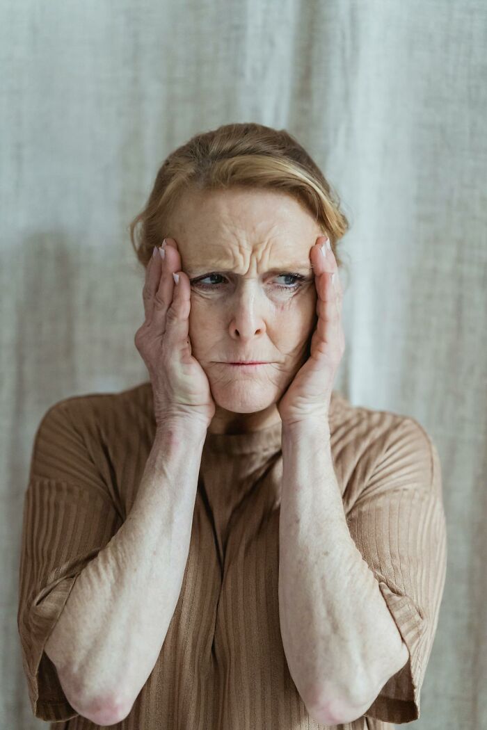 Elderly woman looking distressed, holding her face, conveying intense emotions linked to psych ward experiences.
