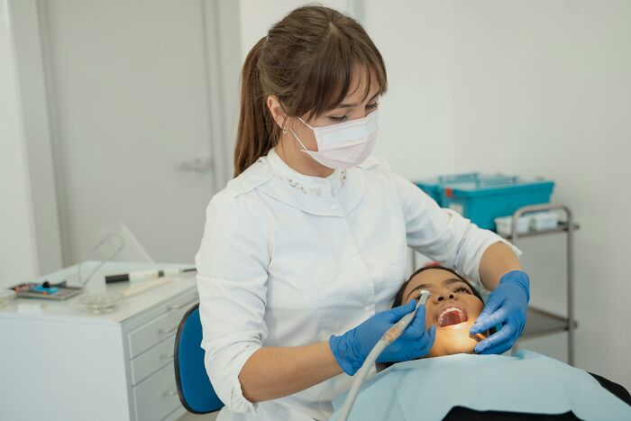 Dentist wearing a mask and gloves cleaning a patient’s teeth showing infuriating examples of work routine resistance.