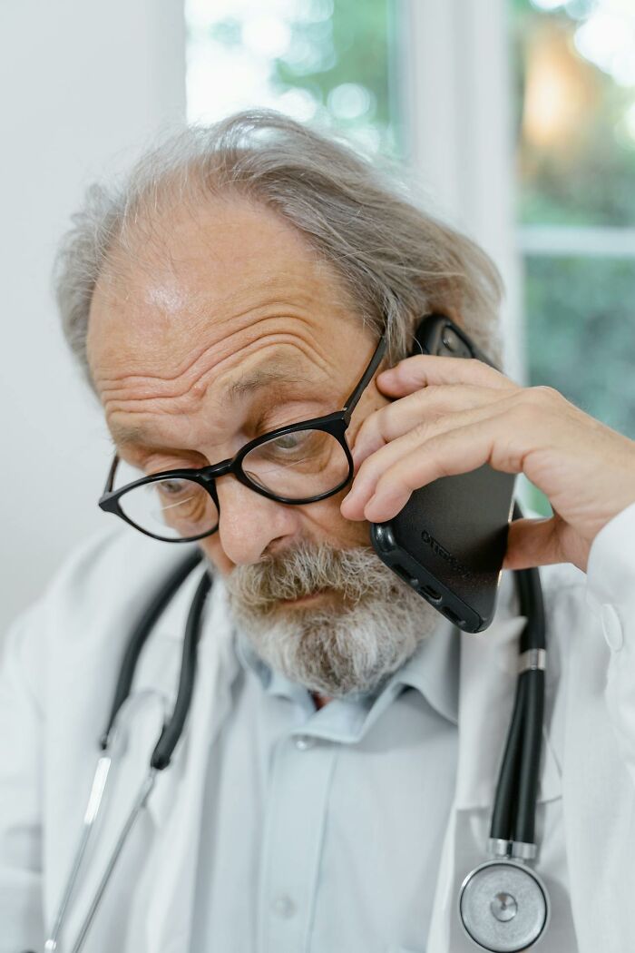 Older male nurse with glasses and stethoscope speaking on phone, representing nurses of psych wards with intense stories.