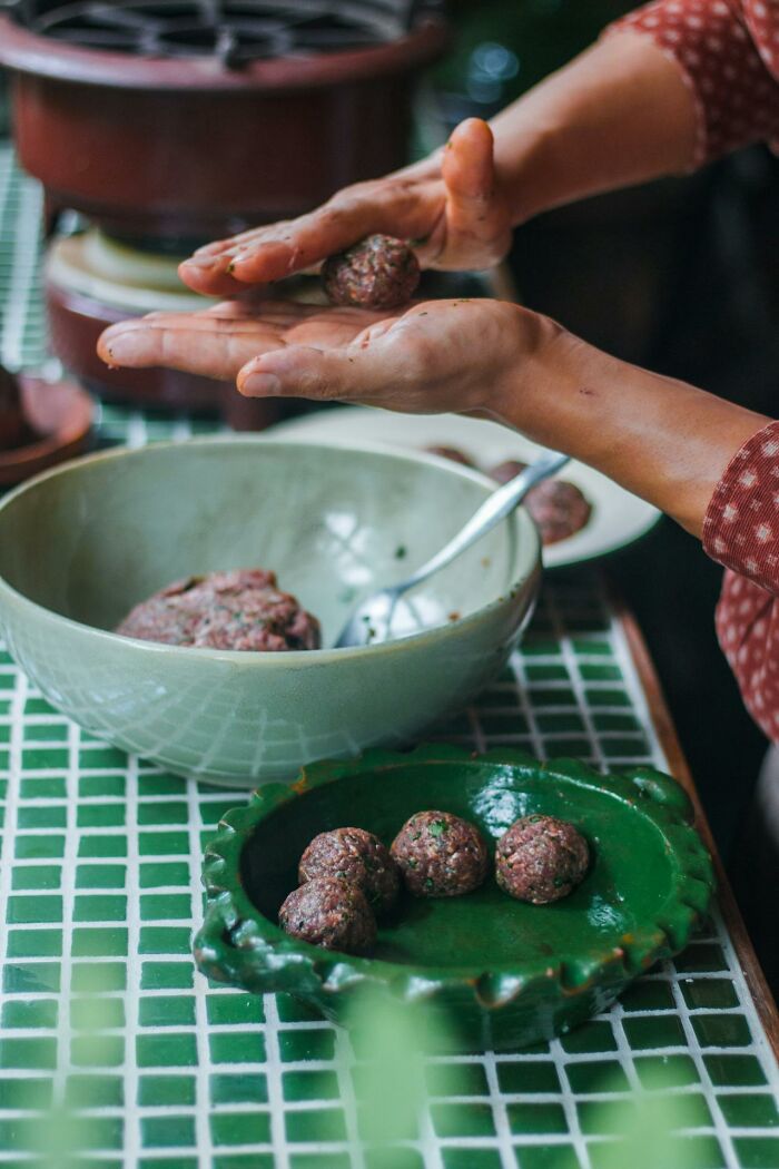 Hands shaping meatballs over a bowl and plate on a green tiled surface, representing heavy confessions theme.