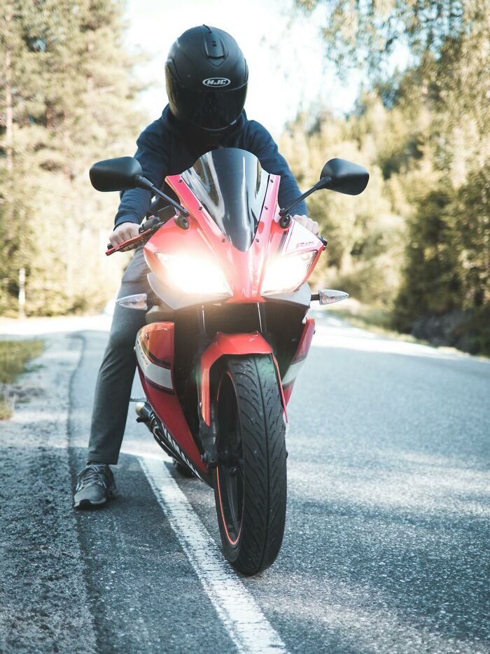 Person wearing helmet on red motorcycle with headlights on, capturing one of the bizarre moments on a forest road.