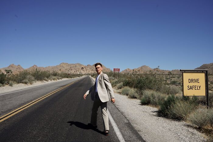 Man in a suit walking on a deserted road near a drive safely sign, evoking haunting things truckers have seen on roads at night.