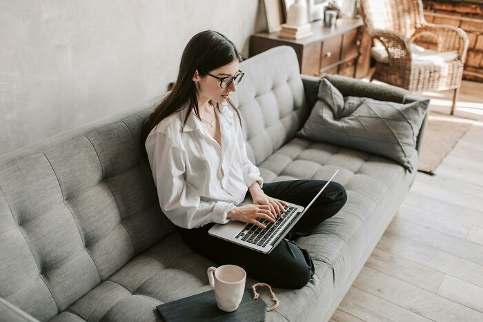 Young woman on sofa using laptop, relatable and guilty of common ridiculous things in a casual home setting