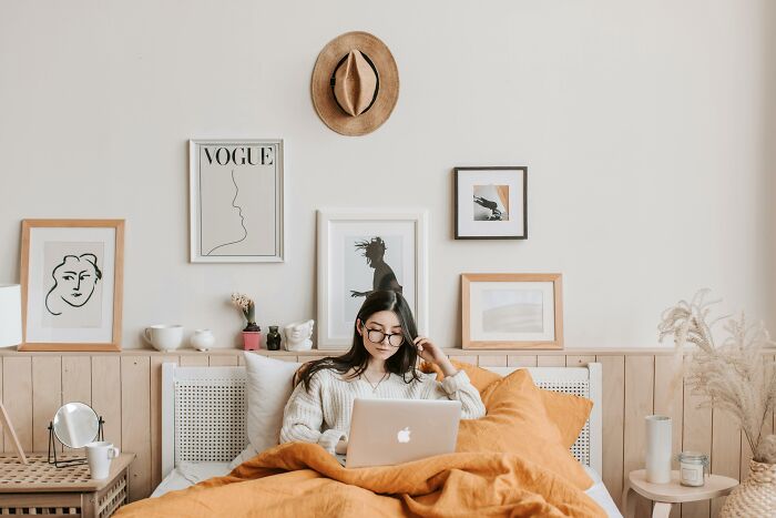 Young woman in cozy bedroom working on laptop, relatable scene showing everyday ridiculous but relatable things people do.
