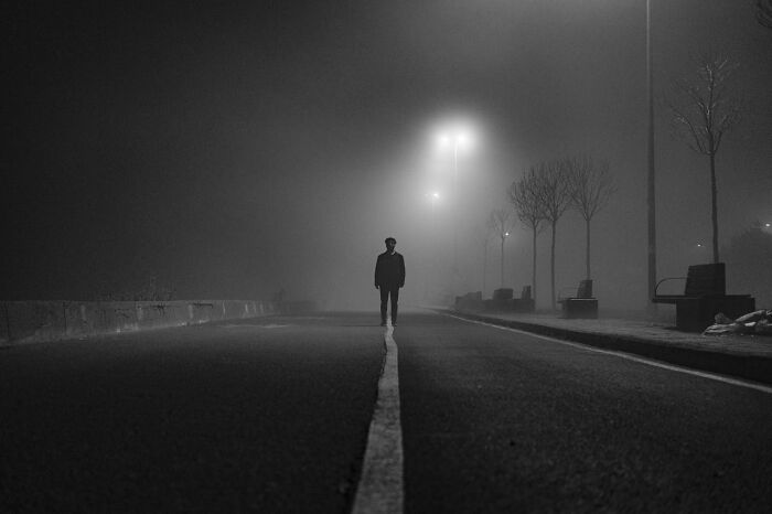Single figure standing on a foggy road at night, evoking haunting scenes truckers have seen on the road at night.