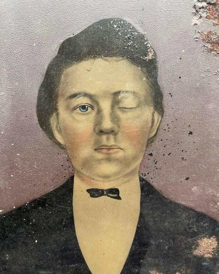 Faded old portrait of a man with one eye closed, a bow tie, and visible signs of age on the surface, showing very old objects.