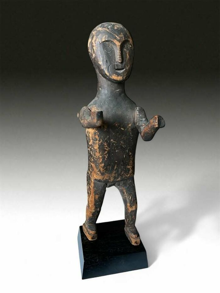 Old wooden figurine standing on a black base representing one of the very old objects that tell stories about ancestors.