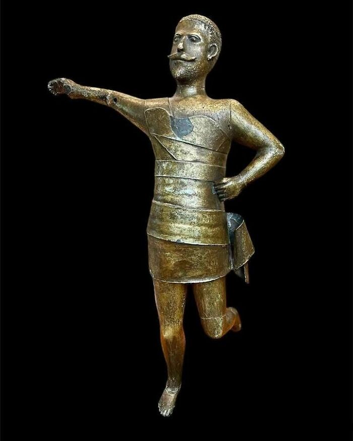 Ancient bronze statue of a warrior in armor with one arm extended, an example of very old objects from ancestors.