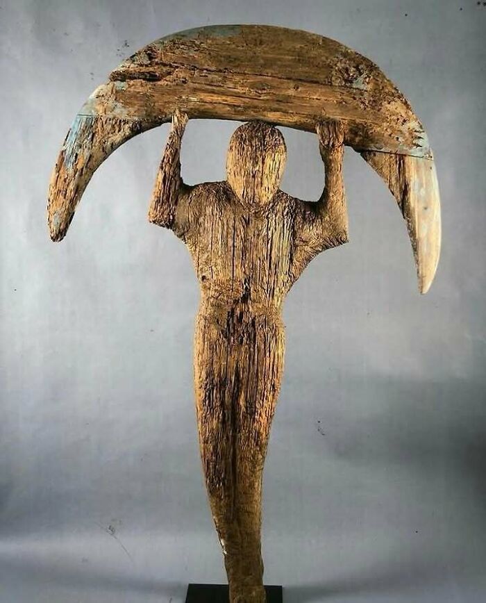 Wooden sculpture of a very old object depicting a human figure holding a crescent shape from ancient ancestors.