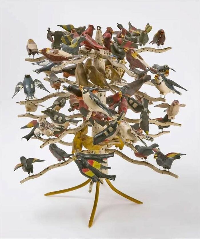 Wooden bird sculpture with multiple colorful carved birds displayed on branches, an old object telling stories of ancestors.