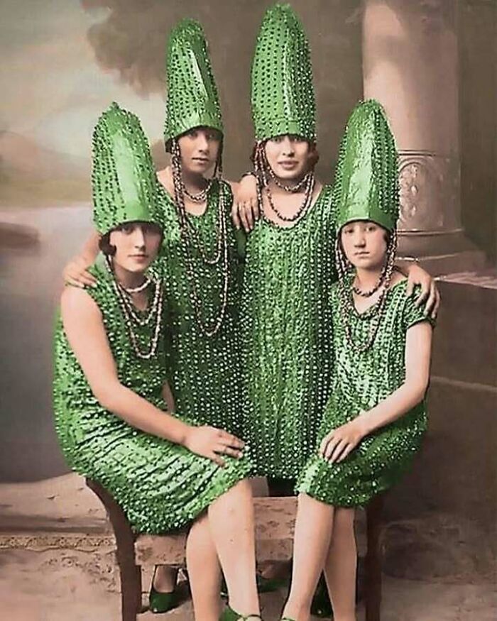Four women in matching vintage green beaded dresses and tall hats, an old object reflecting ancestral fashion history.