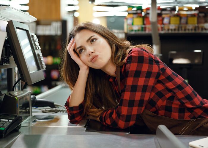 Tired retail employee in a red plaid shirt leaning on the counter during a busy Black Friday shift in a store.