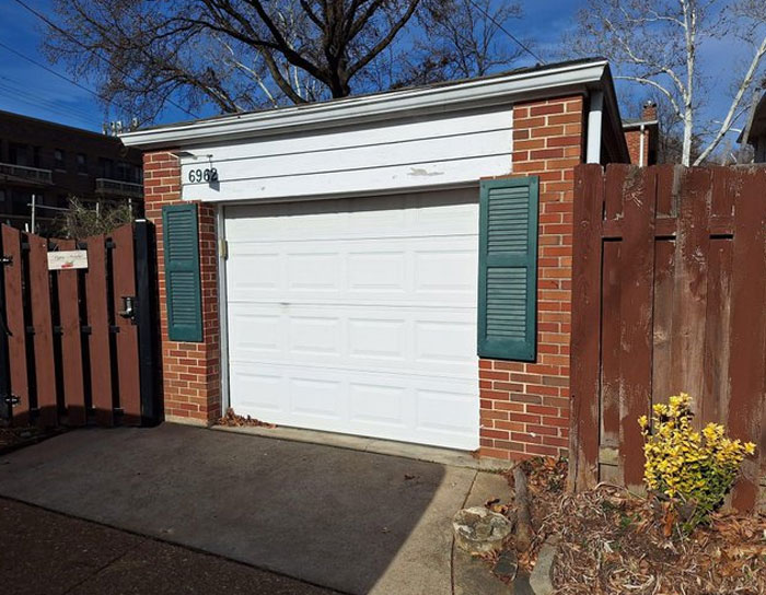 Brick garage with a white door flanked by decorative shutters and a wooden fence, showcasing design and architecture flaws.