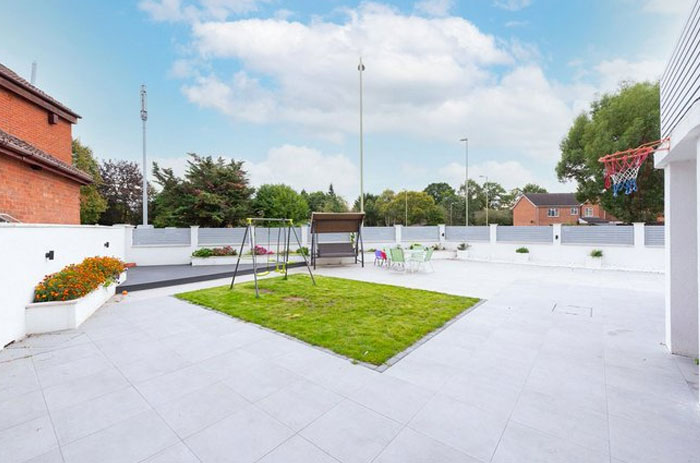 Backyard with small grass patch surrounded by large tiled area showing a design and architecture nightmare.