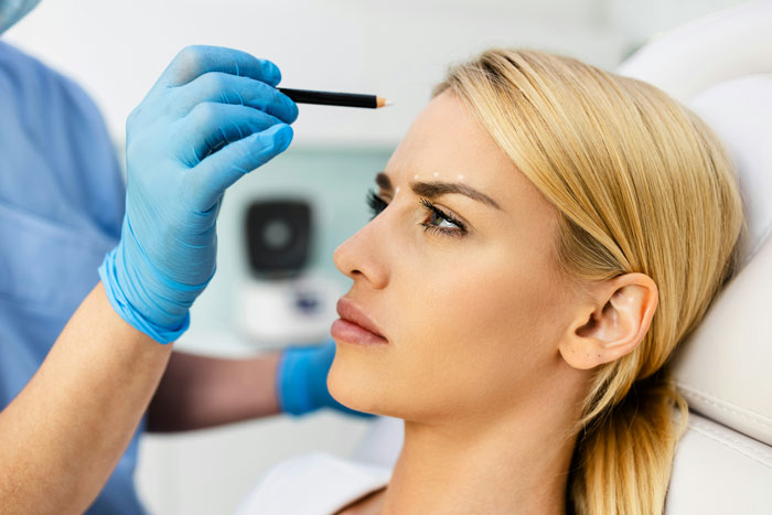 Blonde woman receiving cosmetic consultation with medical professional wearing gloves, discussing possible surgery options.