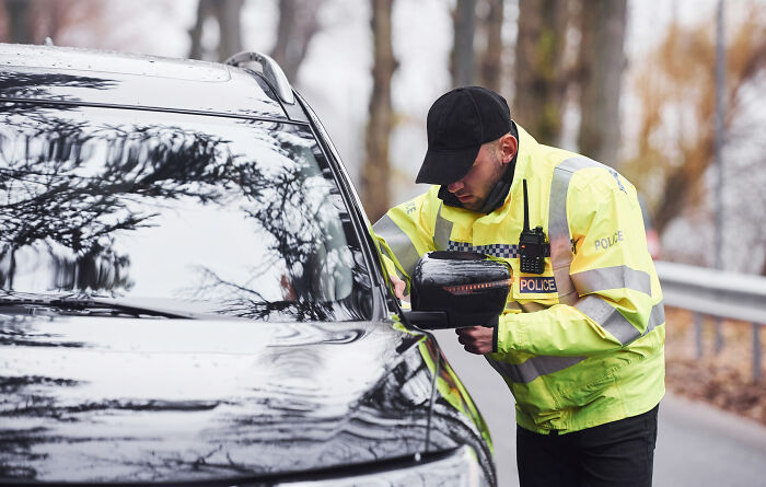 Police officer in a high-visibility jacket checking a driver during a traffic stop, illustrating dumb drivers consequences.