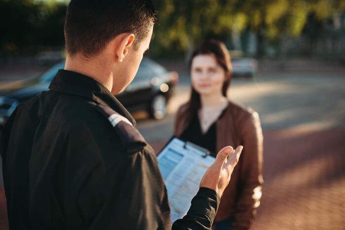 Police officer talking to a woman driver outside with a clipboard, illustrating stories of dumb drivers getting what they deserved.
