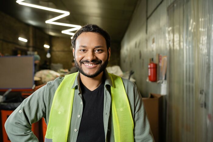 Man wearing a safety vest smiling confidently in a warehouse, illustrating times people fell for scams and their impact.