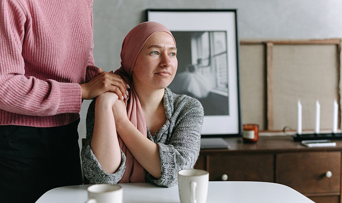 Woman wearing a headscarf looking hopeful while another person offers comfort, illustrating medical bills support and family trust issues.