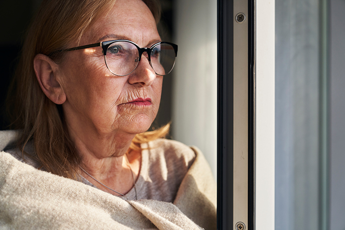 Older woman wearing glasses looking out window with a pouty expression, reflecting a Thanksgiving family conflict. Older woman wearing glasses looking out window with a pouty expression, reflecting a Thanksgiving family conflict.