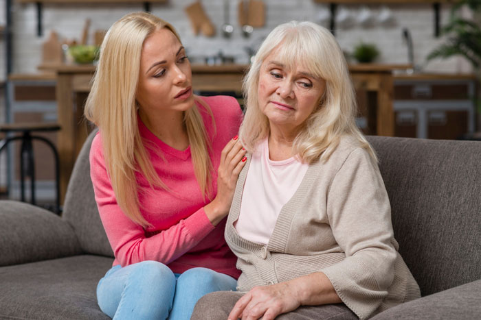 Young pregnant daughter comforting her upset mother on a couch, showing concern and emotional support at home.