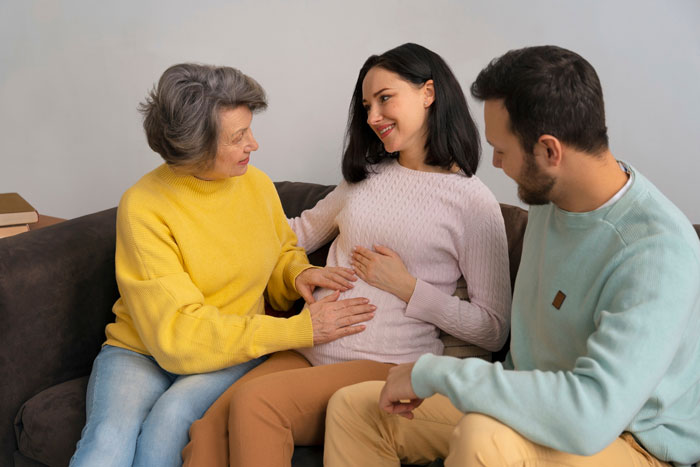 Pregnant daughter smiling while sitting with family on couch, sharing a warm moment at home.