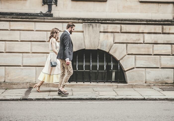 A couple walking along a stone sidewalk near a historic building, illustrating relationship gestures and devotion.