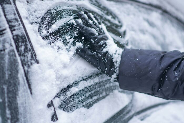 Hand wearing black glove clearing snow off car window, illustrating relationship gestures and princess treatment concept.