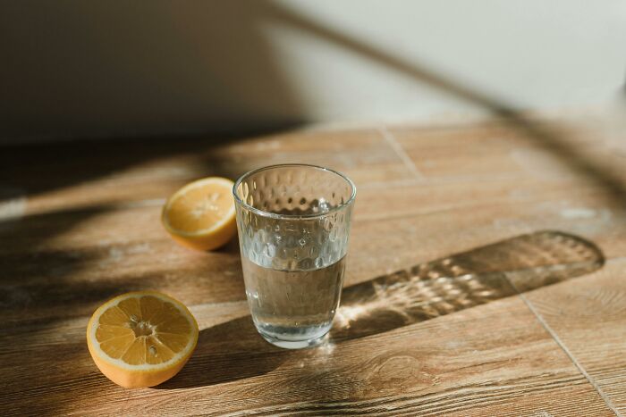 Glass of water with lemon halves on wooden table casting shadows, symbolizing relationship gestures and princess treatment.