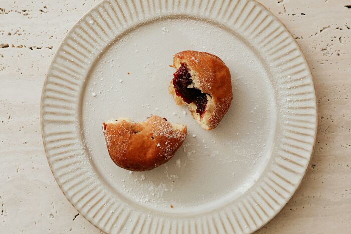 Half-eaten jam-filled pastry on a white plate with powdered sugar highlights relationship gestures concept.