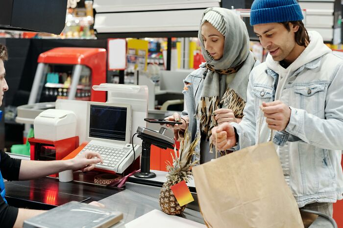 A couple using a phone to pay at checkout while a cashier bags groceries, illustrating relationship gestures.