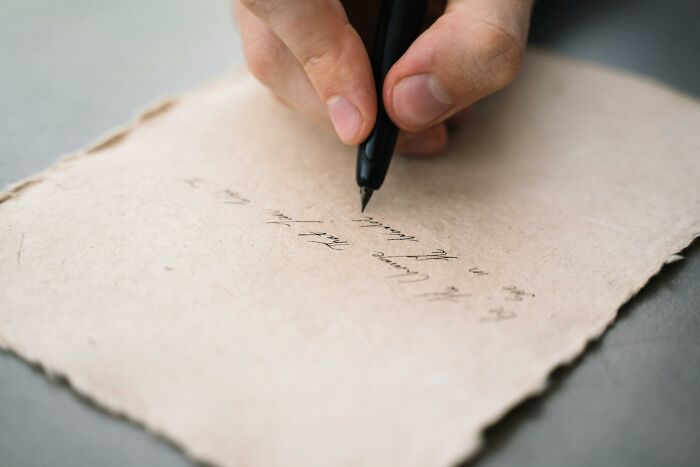 Close-up of a hand writing a romantic note on textured paper, illustrating relationship gestures and princess treatment.