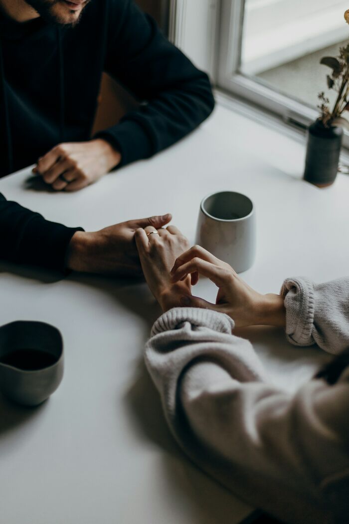 Couple holding hands across a table with coffee mugs, reflecting on harsh truths about marriage and its reality.