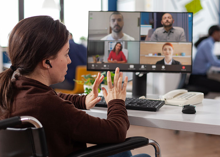 Woman in wheelchair using psychological tricks during a video call with colleagues in a modern office setting.