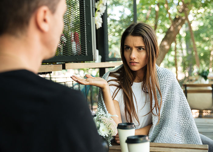 Woman using psychological tricks in a serious conversation with a man at an outdoor café on a sunny day.