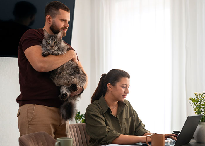 Man holding a cat watching woman focused on laptop, illustrating psychological tricks people use on themselves and others.