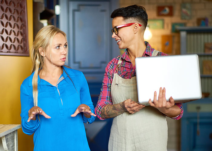 Two women discussing psychological tricks while one shows a laptop, illustrating psychological tricks people use on themselves and others.