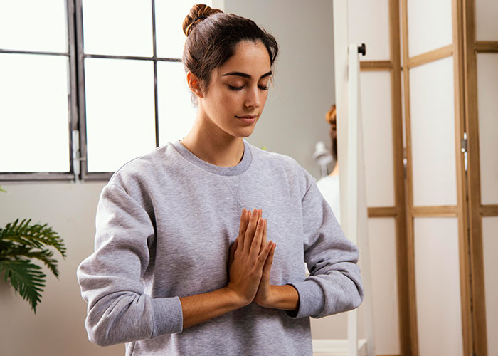 Young woman practicing mindfulness meditation indoors, demonstrating psychological tricks people use on themselves for mental well-being.