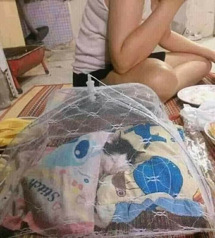 Small animal wrapped in colorful blankets inside a mesh net while person sits nearby on a patterned floor indoors.