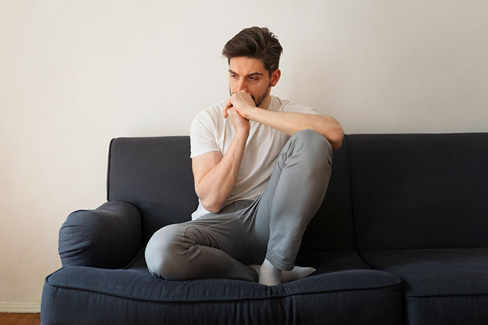 Young man sitting on a sofa looking thoughtful and unhappy, representing parents and children sharing honest reasons for unhappiness.
