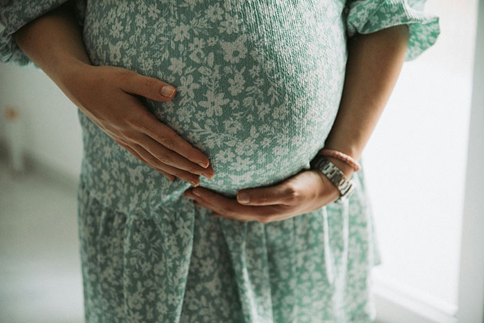 Pregnant woman in a green floral dress holding her belly, illustrating parents and children relationships and unhappiness reasons.
