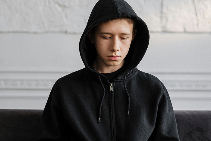 Teen boy in a black hoodie looking down with a somber expression, reflecting parents and children unhappiness reasons.