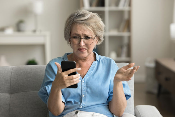 Woman upset holding phone, reacting emotionally while sitting on couch in a cozy living room setting. Woman upset holding phone, reacting emotionally while sitting on couch in a cozy living room setting.