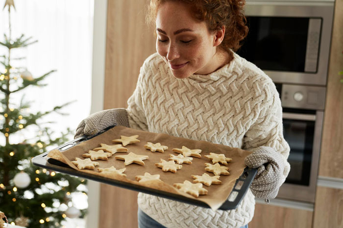 A woman holding a baking tray with freshly baked cookies, smiling proudly after perfecting secret cookie recipe. A woman holding a baking tray with freshly baked cookies, smiling proudly after perfecting secret cookie recipe.
