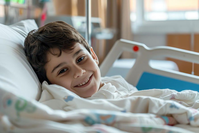 Smiling boy lying in hospital bed, appearing nonverbal and bedridden, in a medical care setting.