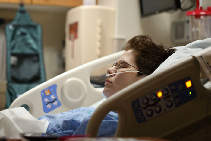 Nonverbal, bedridden boy lying in hospital bed with oxygen tube, appearing to rest in a medical care setting.