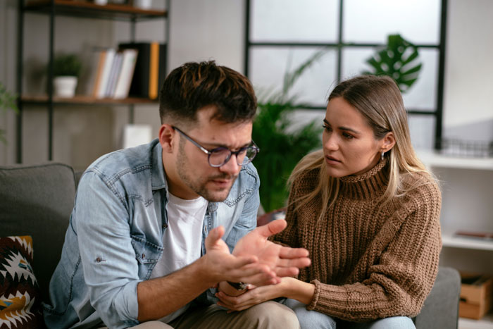 Man refuses babysitting on vacation, woman looks concerned during serious conversation in cozy living room.